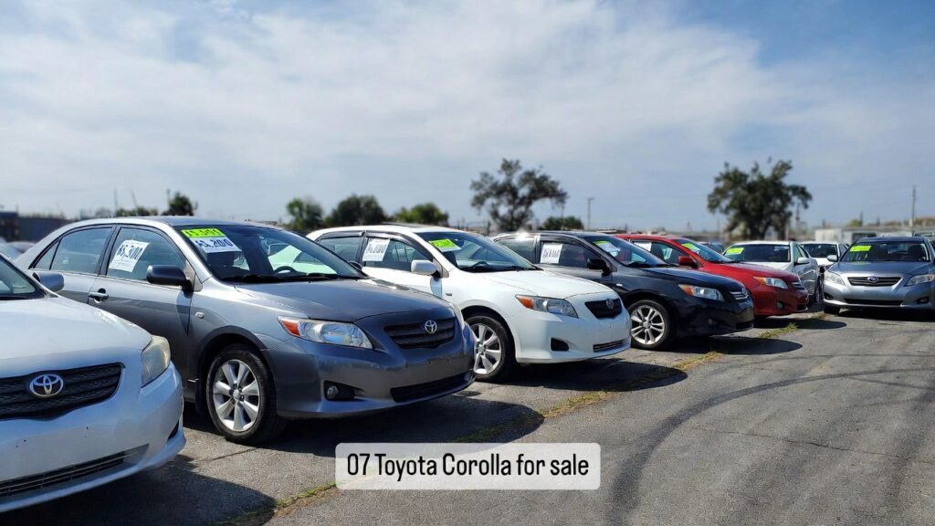 Photo of several 2007 Toyota Corolla cars parked on a used car lot with visible price tags, representing current market value