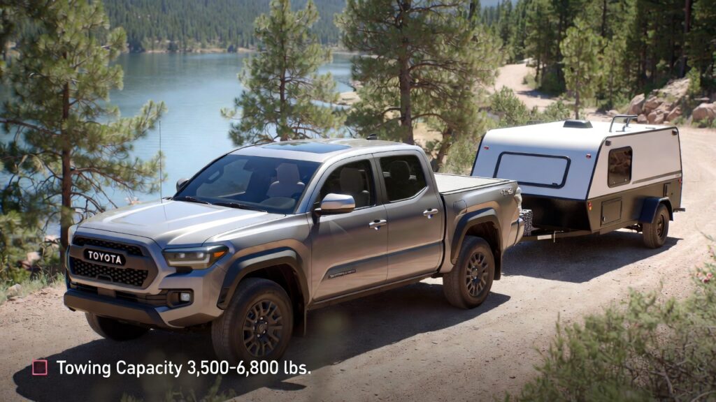 Silver Toyota Tacoma towing small camper trailer with tow package at lakeside.
